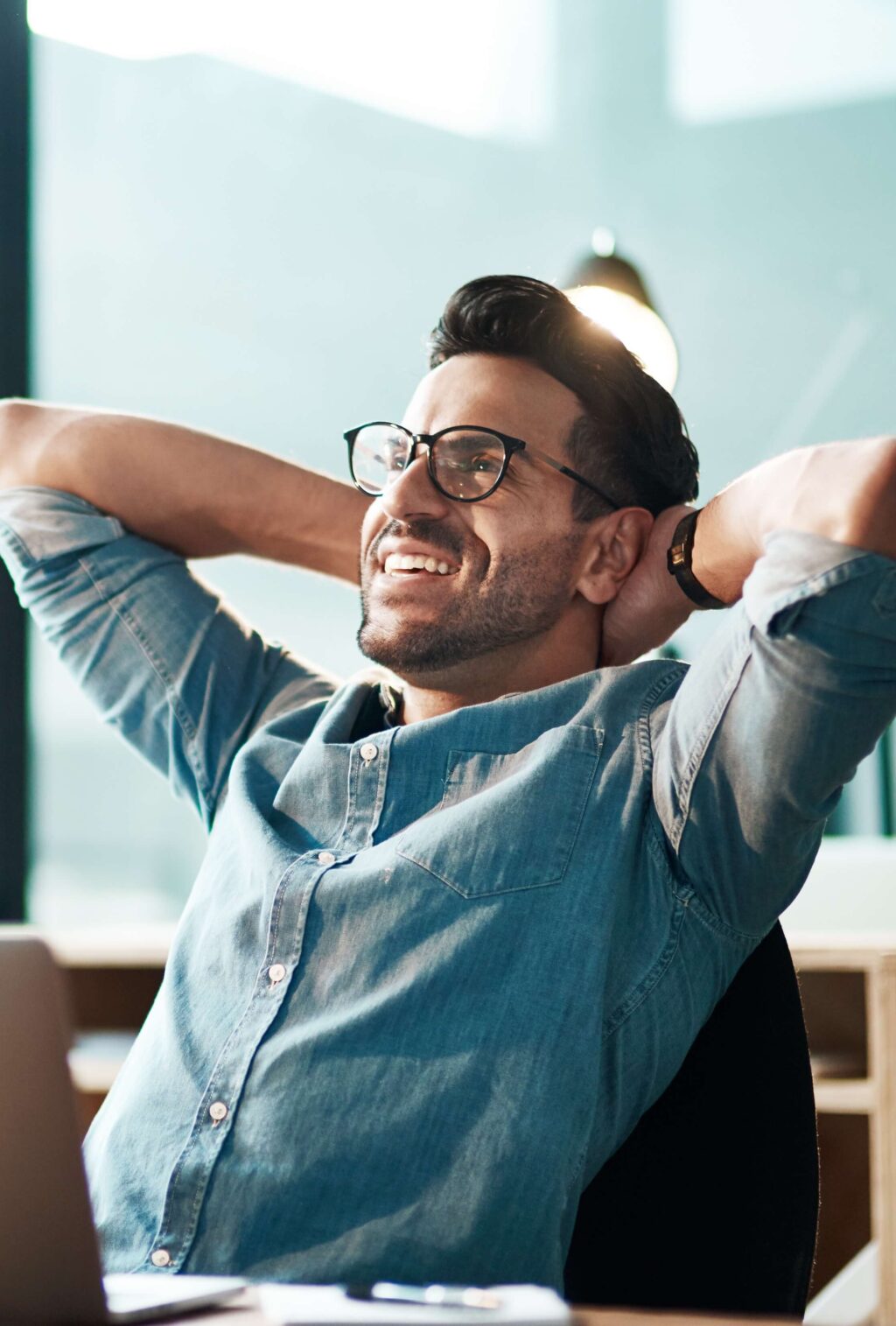 Mann mit Brille entspannt am Schreibtisch, l&auml;chelnd, mit Laptop. Fokus auf positive Arbeitsatmosph&auml;re. Climate Energy.
