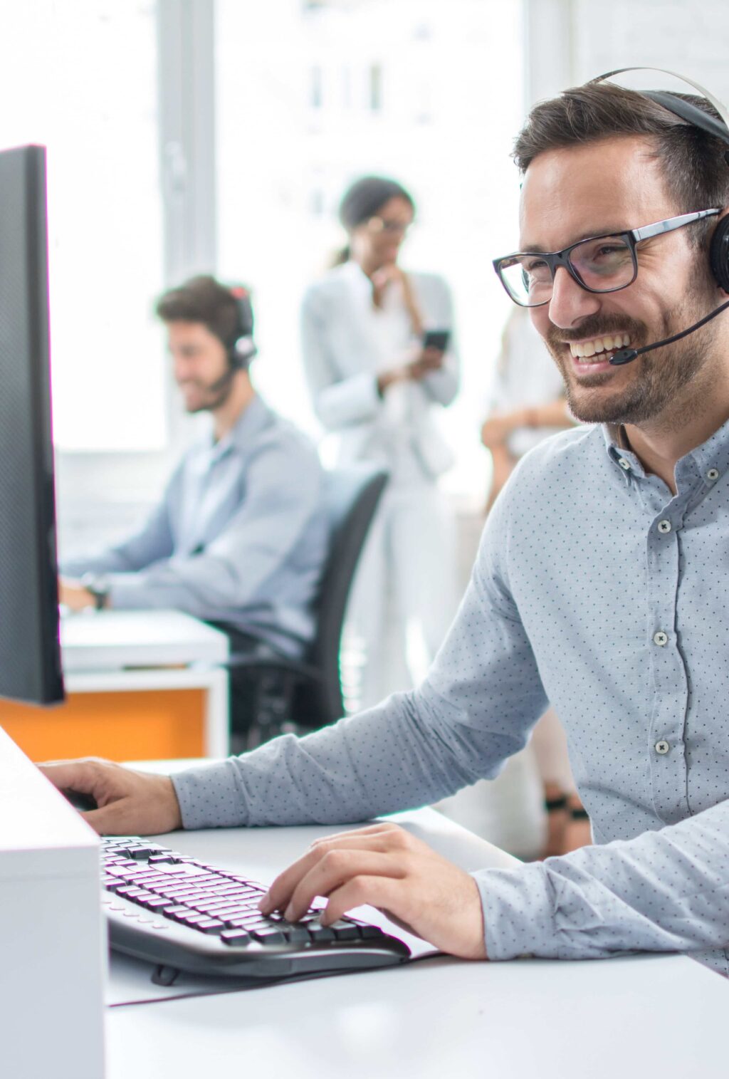Ein l&auml;chelnder Mann mit Kopfh&ouml;rern arbeitet am Computer in einem modernen B&uuml;ro. Climate Energy.